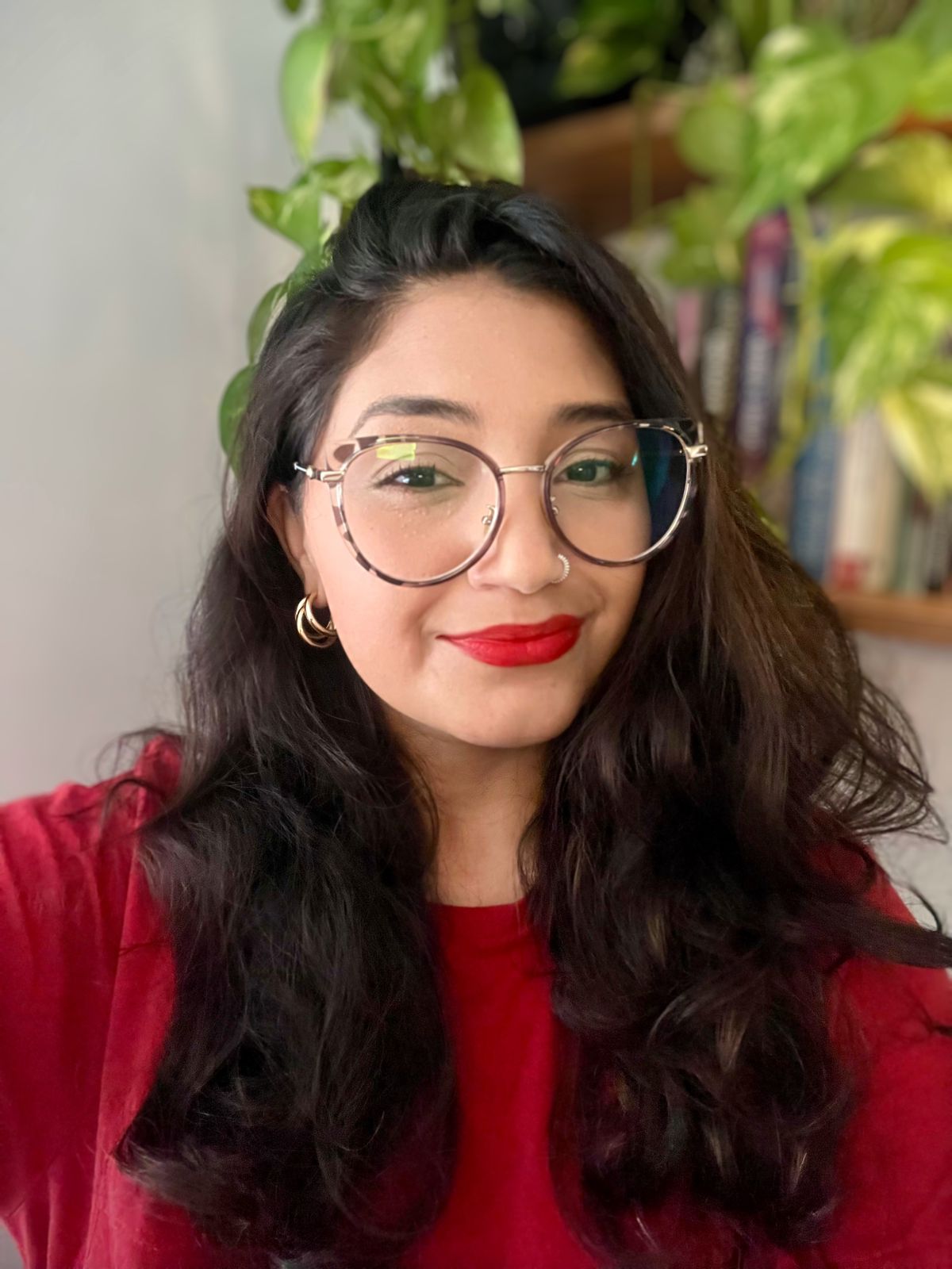 Mayara Gaspar, psicóloga, diante de uma estante com livros e plantas